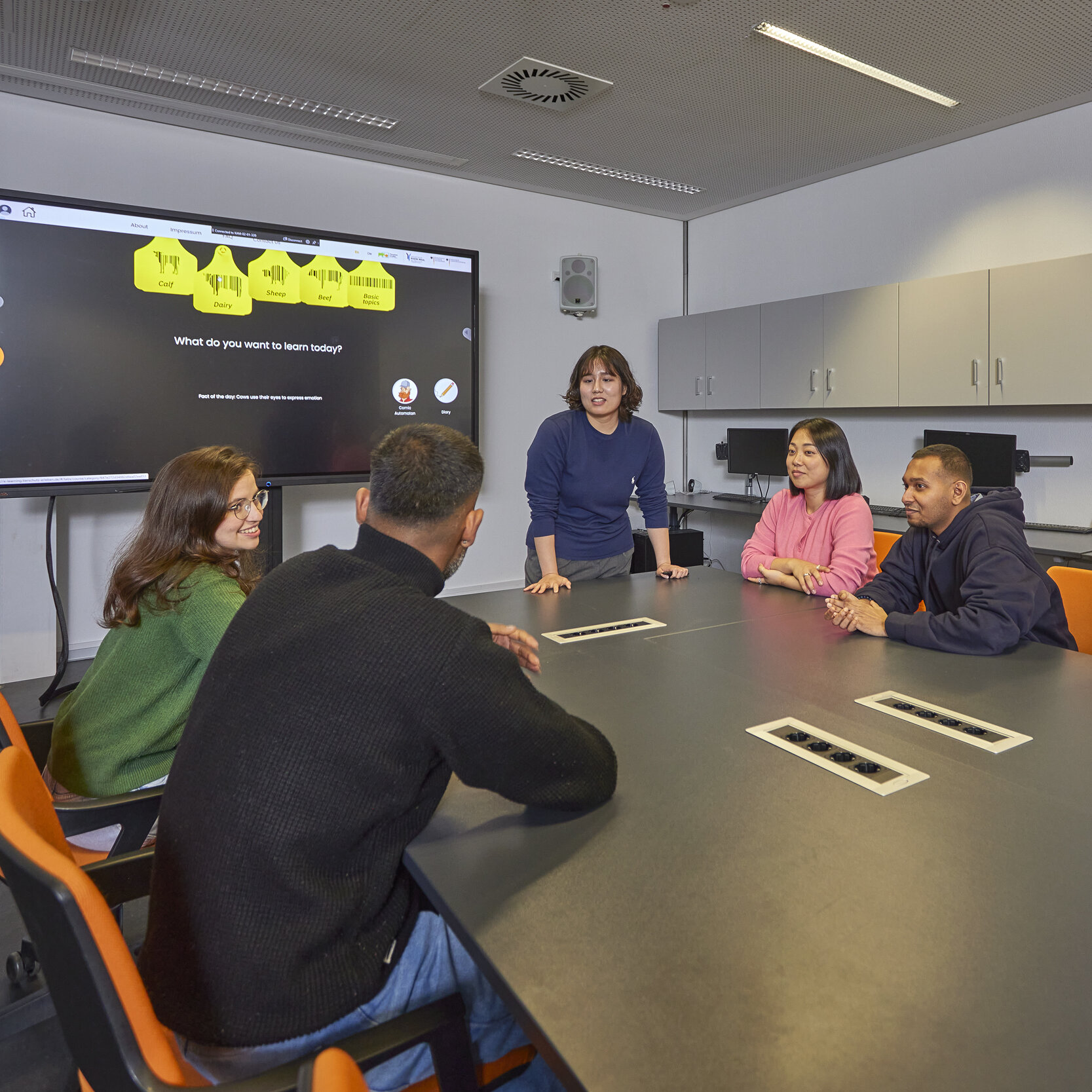 Studentin präsentiert ihr Projekt vor einer Gruppe Studierender am Tisch