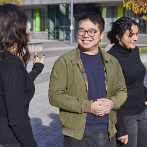Drei Studierende stehen auf dem Campus und unterhalten sich angeregt