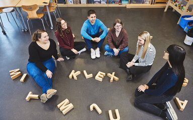 Praxisnah Studierende des Studiengangs Kindheitspädagogik sitzen auf dem Boden und haben aus Buchstaben auf dem Boden das Wort KLEX gelegt