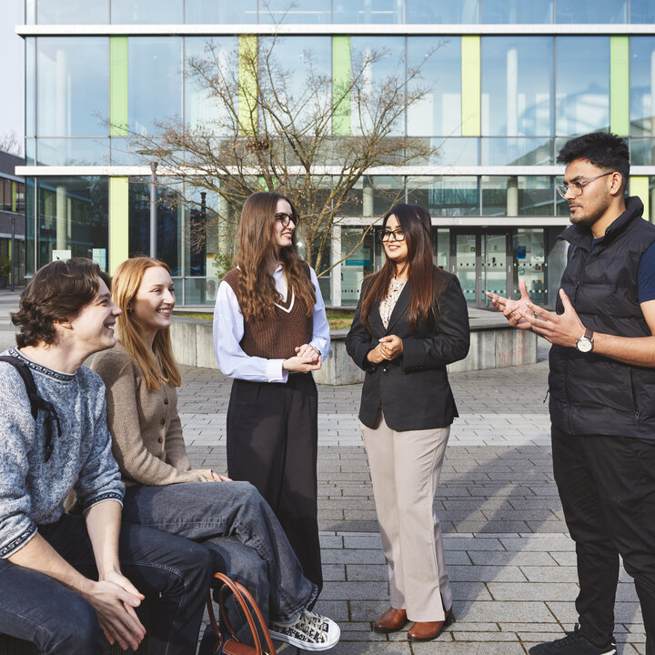 Fünf Studierende treffen sich am Campus Kamp-Lintfort mit Gebäude 1 im Hintergrund