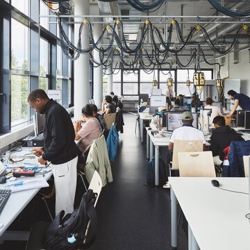 Großer Computerraum mit Studierenden an verschiedenen Tischen, die an verschiedenen Projekten arbeiten. 