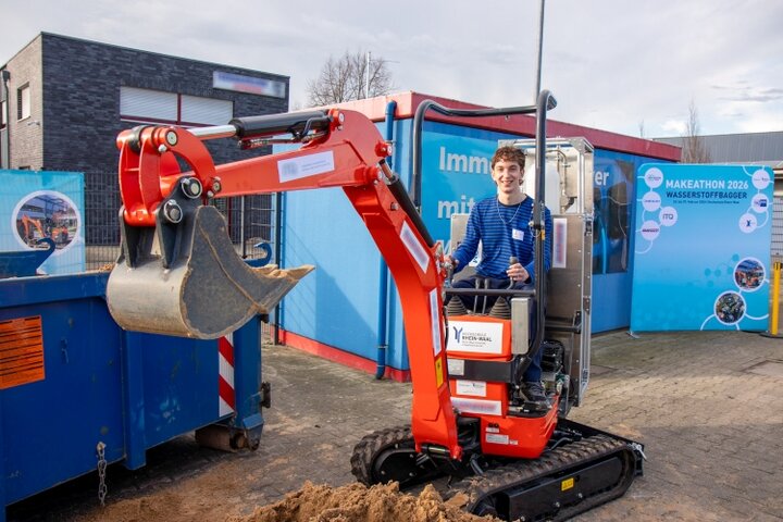 Makeathon-Teilnehmer auf dem umgebauten Wasserstoffbagger