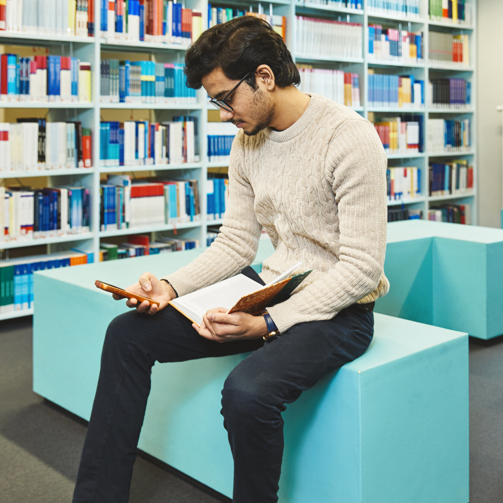 Ein Student sitzt in der Bibliothek Kleve und schaut auf sein Handy
