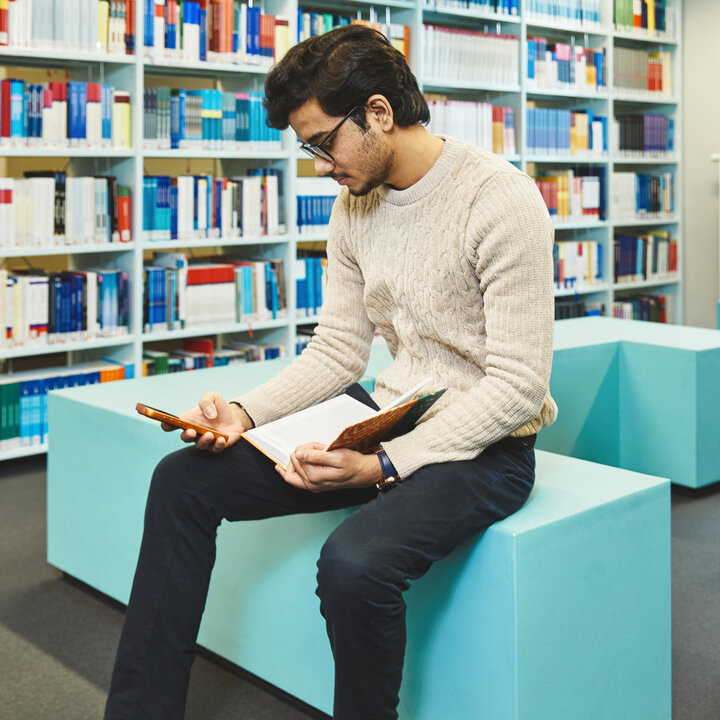 Ein Student sitzt in der Bibliothek Kleve und schaut auf sein Handy
