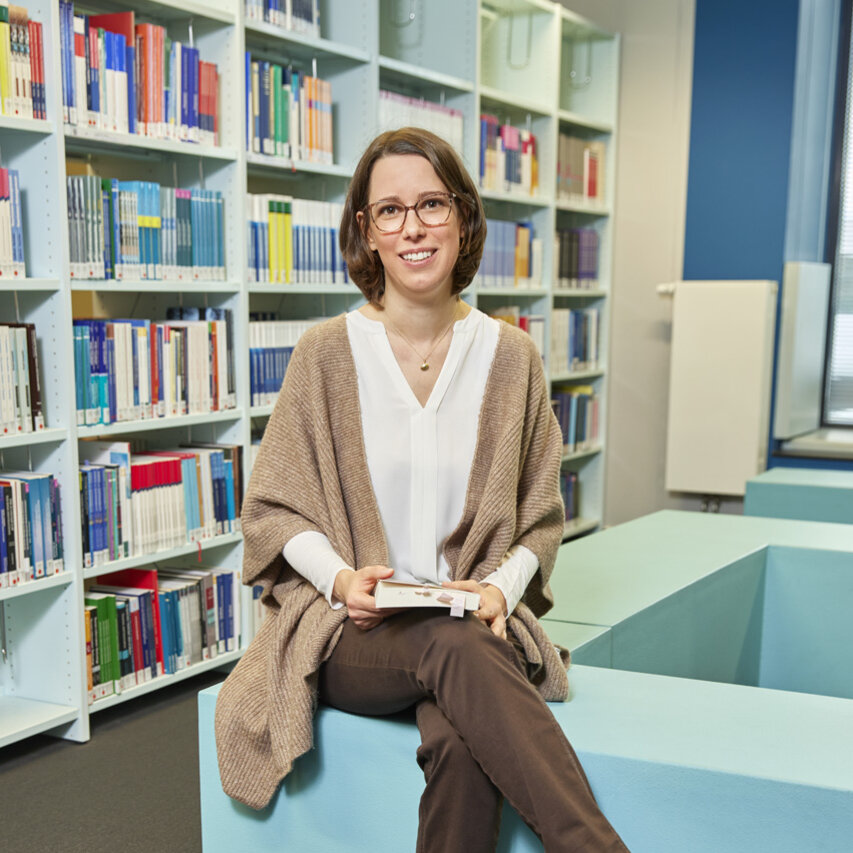 Professorin Titze sitzt in der Bibliothek und hält ein Buch fest.