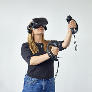 A student is wearing a VR headset and operating two controllers with her arms outstretched.