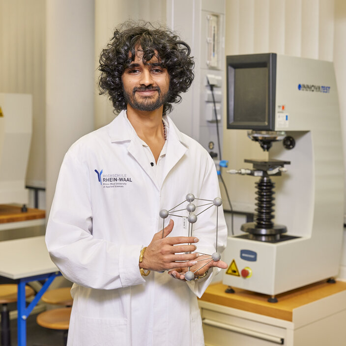 Rudra Ein Studierender steht in einem weißen Kittel in einem Chemielabor und lächelt in die Kamera.