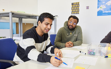 Von Frust zu Flow Zwei Studierende arbeiten gemeinsam an einem Tisch mit Papier, Stiften und weiteren Arbeitsmaterialien.