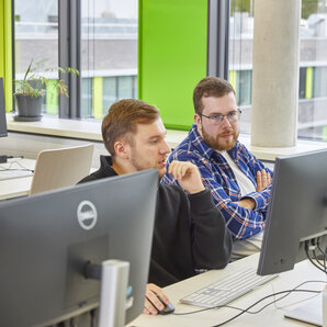 Zwei Studierende sitzen an Computerarbeitsplätzen und schauen auf einen Bildschirm.