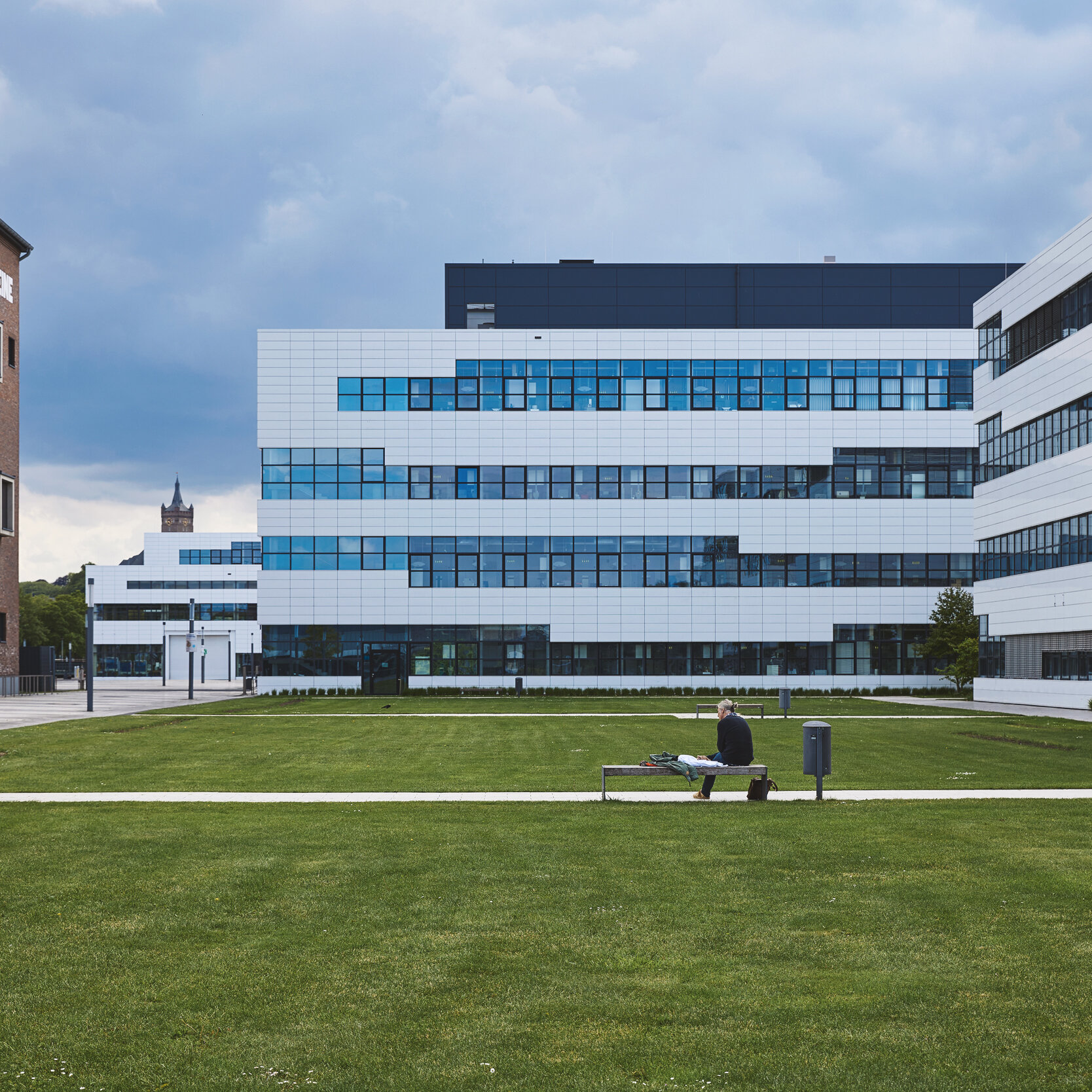 Standort Kleve: im Vordergrund ist eine große Rasenfläche. Links ist die Bibliothek, ein hohes Gebäude aus Backsteinen mit Giebeldach. Geradeaus und rechts sind moderne Gebäude mit vielen Fenstern.