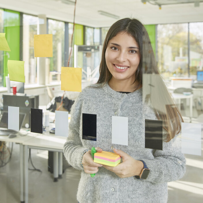 Ana-Sofia Esparaza-Santaella aus Mexiko Porträt von Ana-Sofia Esparaza-Santaella, Studentin aus Mexiko, posiert im FabLab hinter einer Glaswand mit Haftnotizen.