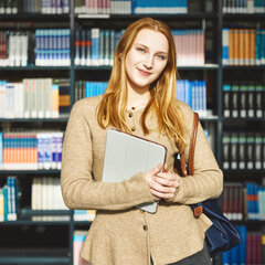 A student is standing in the Kamp-Lintfort library with her laptop