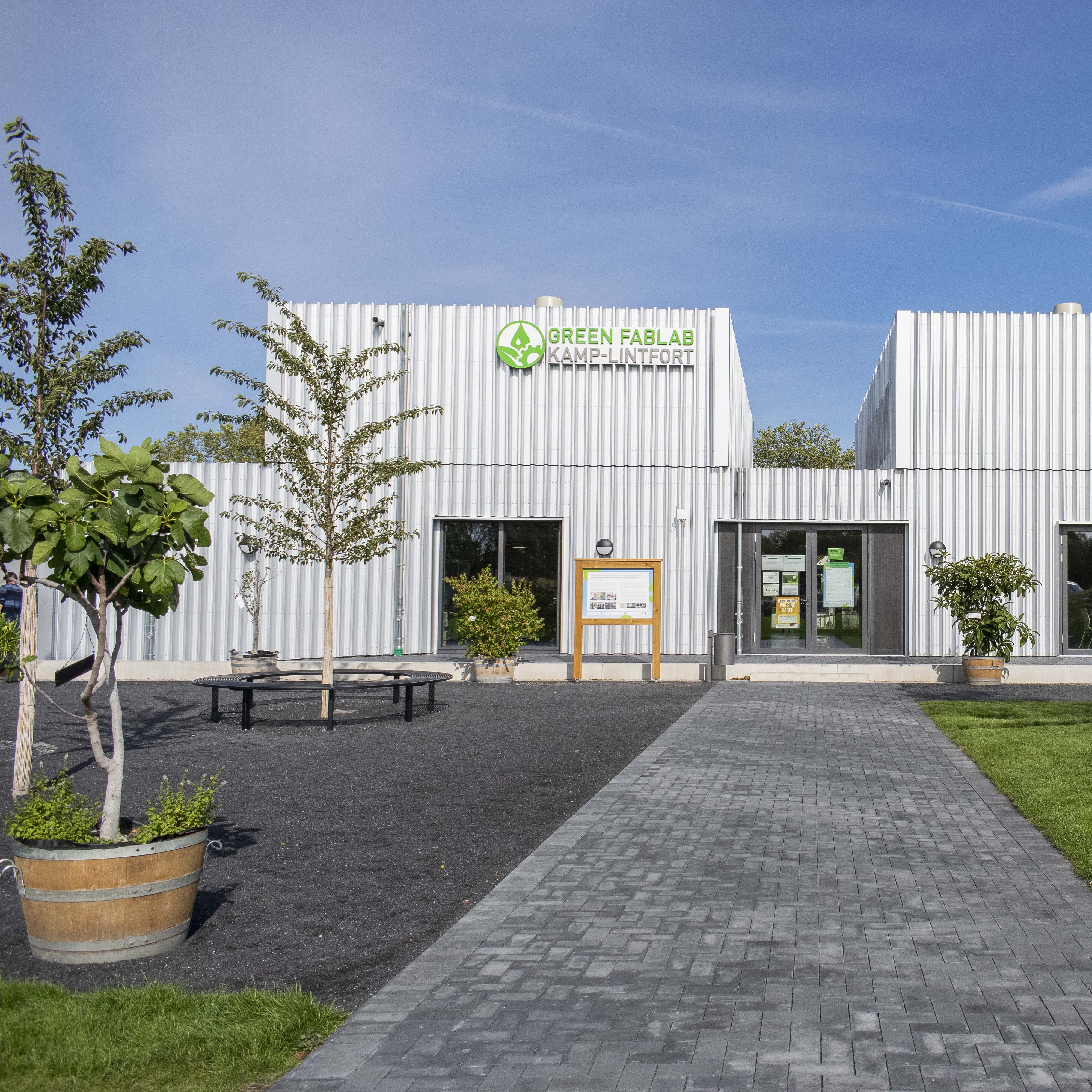 Außenansicht des Green FabLab Kamp-Lintfort mit Eingangsbereich, Grünflächen und Bäumen.