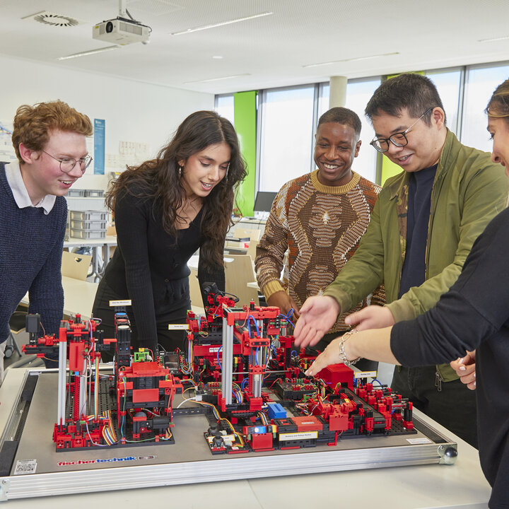Six students are working together on a model factory comprising various technical modules.