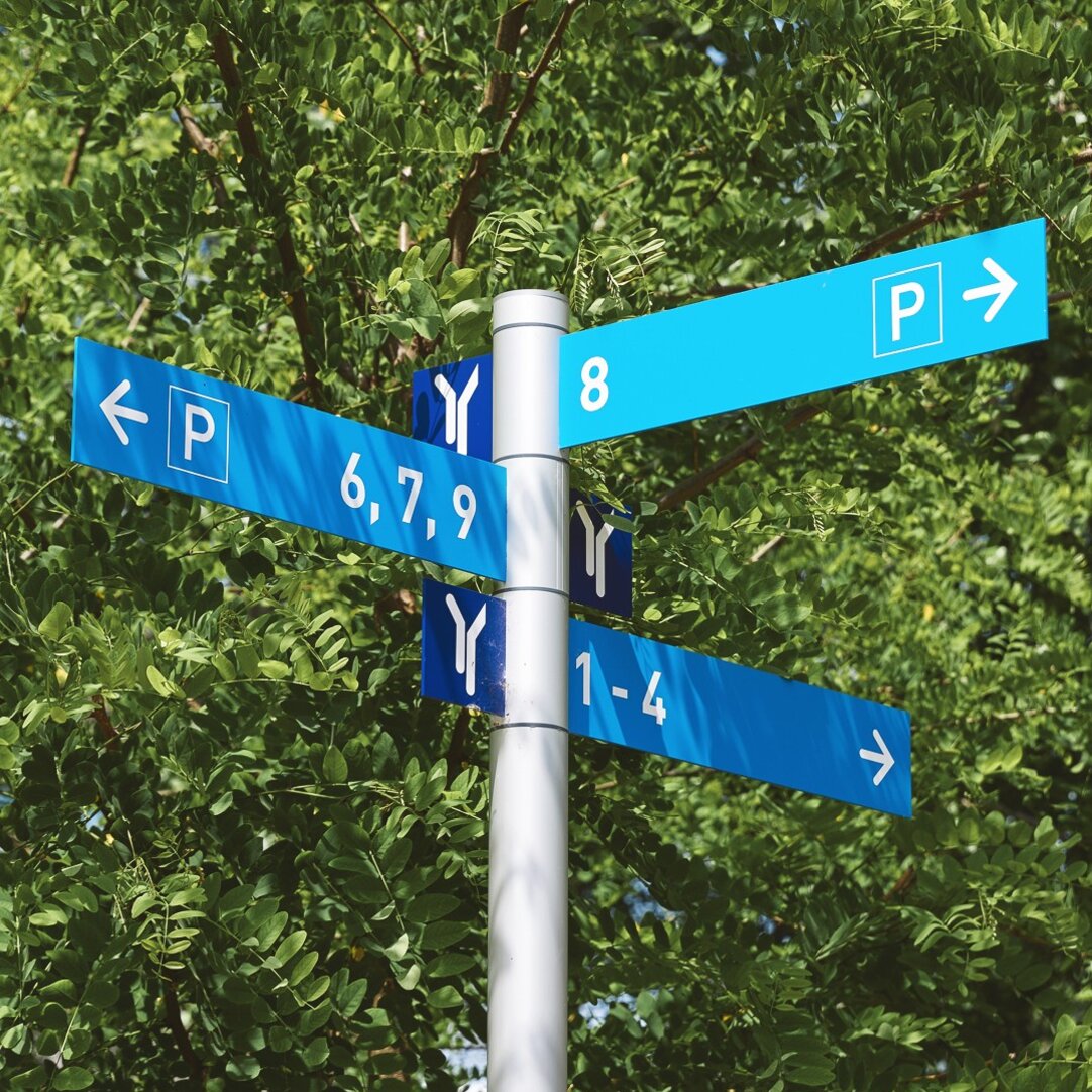 Wegweiser der Hochschule Rhein Waal, auf dem Schilder in drei verschiedene Richtungen zeigen und den Weg in Richtung der Gebäude 1 bis 9 weisen.
