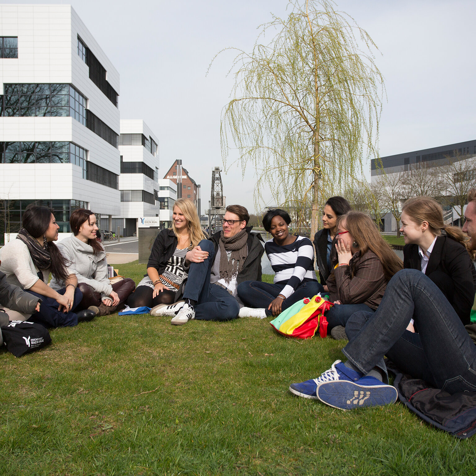 Eine Gruppe Studierender sitzen auf dem Rasen auf dem Campus Kleve