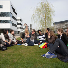 Eine Gruppe Studierender sitzen auf dem Rasen auf dem Campus Kleve