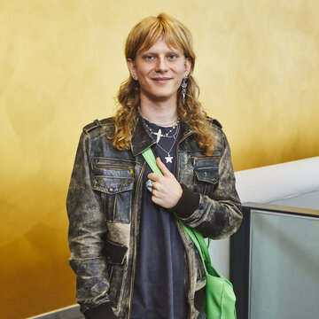 Person mit langen Haaren steht im Audimax und schaut in die Kamera.