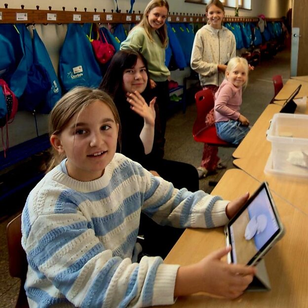 Schülerin mit tablet am Tisch sitzend schaut in die Kamera