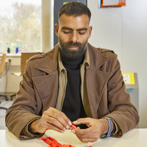 Student sitzt an einem Tisch im Fab Lab und formt eine rote Knetfigur.