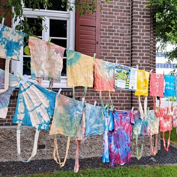 Auf zwei Wäscheleinen zwischen Bäumen hängen bunte Batik-Jutetaschen.