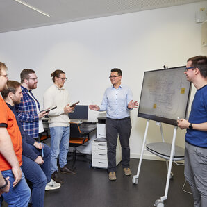 Eine Gruppe Studierender diskutiert über ein Projekt vor einer Stelltafel