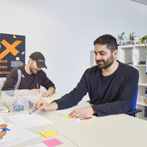 Mehrere Studierende arbeiten gemeinsam an einem Tisch mit Papier, Stiften und bunten Notizzetteln.