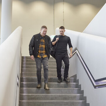 Professor Pfeiffer läuft gemeinsam mit einem Studierenden eine Treppe hinunter. Sie führen ein Gespräch.