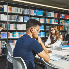 Fünf Studierende sitzen an Arbeitsplätzen oder stehen an den Bücherregalen im Lesesaal der Bibliothek Kamp-Lintfort