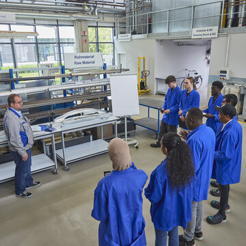Studierende mit Lehrenden stehen in einer Technikhalle auf dem Campus.