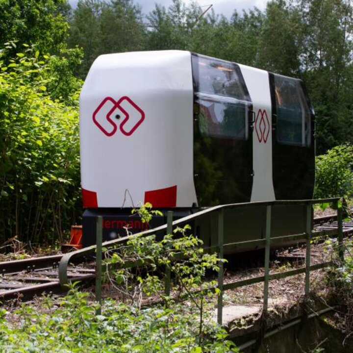 Ein autonom fahrendes Schienenfahrzeug ist auf Bahngleisen. Es ist weiß und hat an den Seiten zwei durchsichtige Türen.