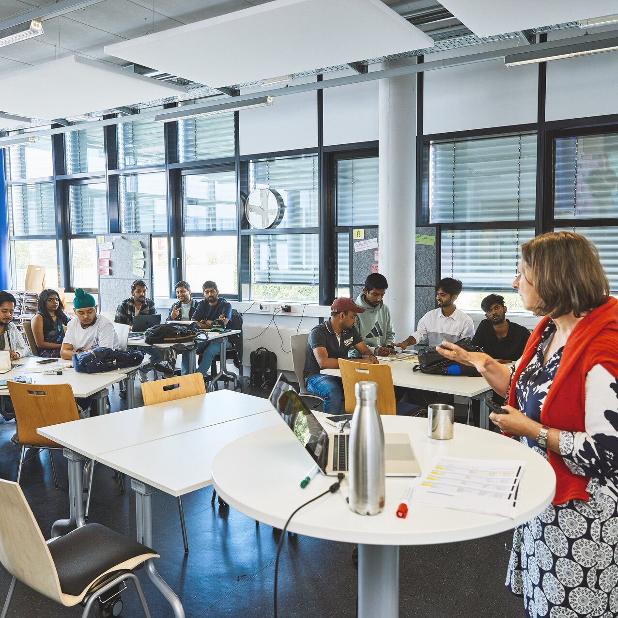Eine Lehrende steht vor einer Gruppe Studierender in einem Seminarraum.