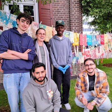 Eine Gruppe Studierender steht mit Professorin vor Wäscheleinen mit Batik-Stofftaschen.