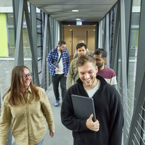 Mehrere Studierende gehen gemeinsam durch einen verglasten Gang auf dem Campus.