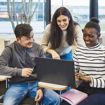 Drei Studierende am Laptop - Teamwork und Projektarbeit Drei Studierende unterschiedlicher Herkunft sitzen im Hörsaal zusammen. Sie schauen gemeinsam lachend auf einen Laptop und besprechen Studieninhalte.