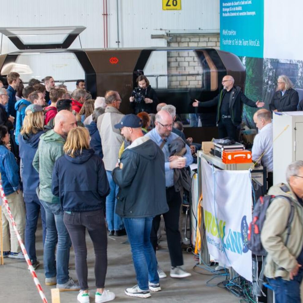 Viele Menschen stehen auf einem Bahnsteig vor dem selbstfahrenden Schienenfahrzeug
