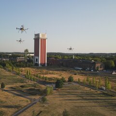 Drei Drohnen fliegen über das alte RAG-Gelände. Im Hintergrund ist ein großer Förderturm zu sehen.