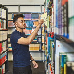 Ein Student nimmt in der Bibliothek Kamp-Lintfort ein Buch aus einem Bücherregal