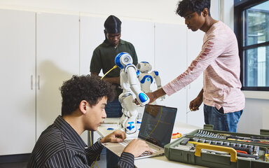 Digitale Kompetenz Drei Studierende arbeiten an einem Roboter.