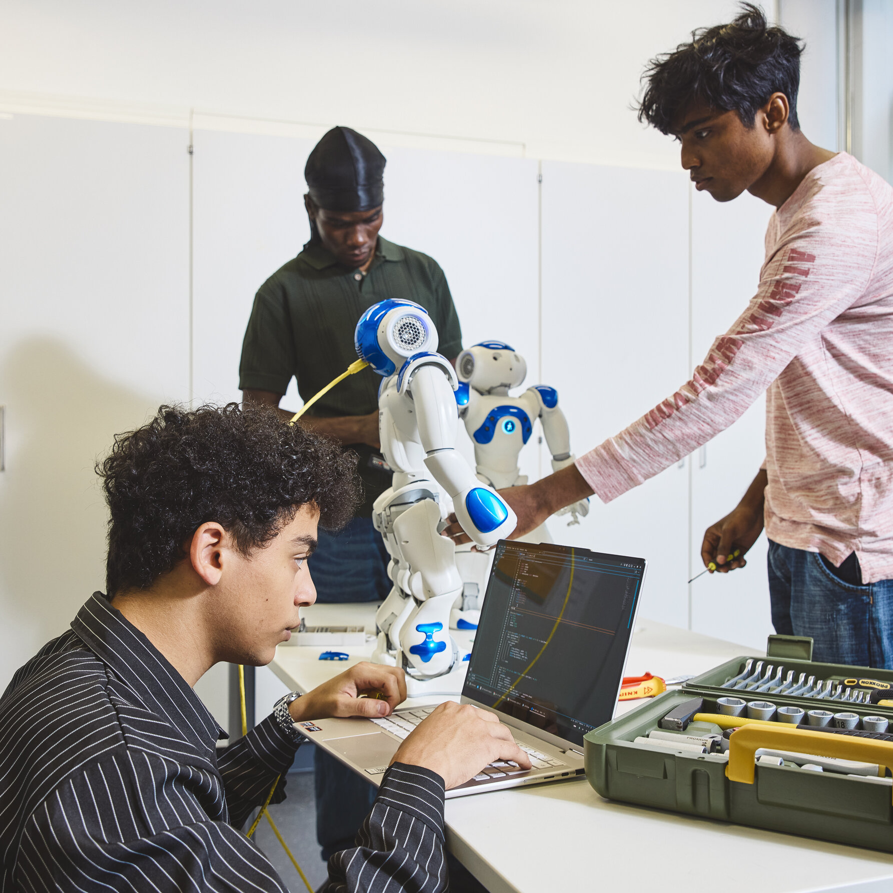Drei Studierende arbeiten an einem Roboter.