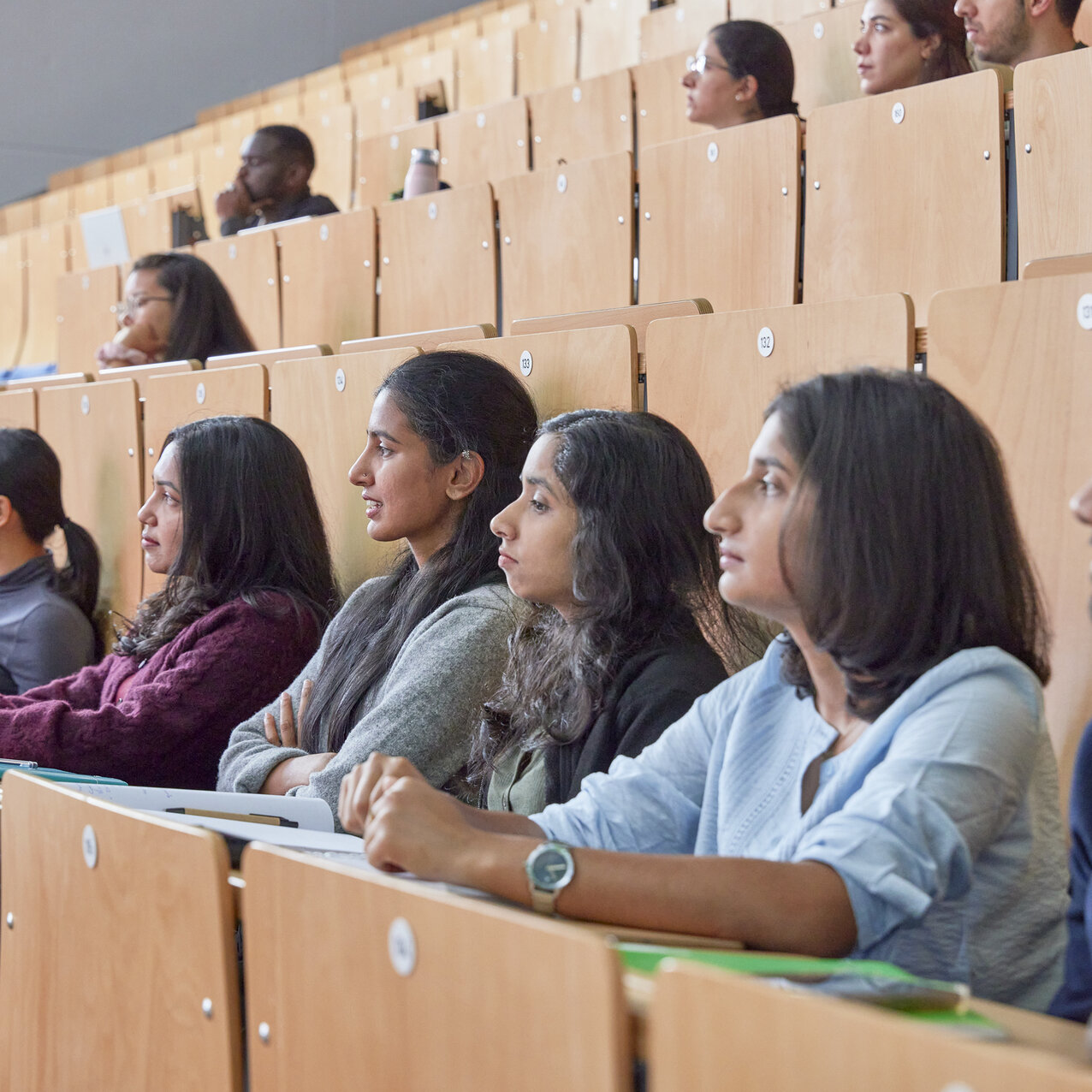Mehrere Studierende sitzen konzentriert in einer Reihe im Hörsaal.