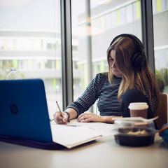 Studentin sitzt vor einem Laptop und schreibt etwas auf