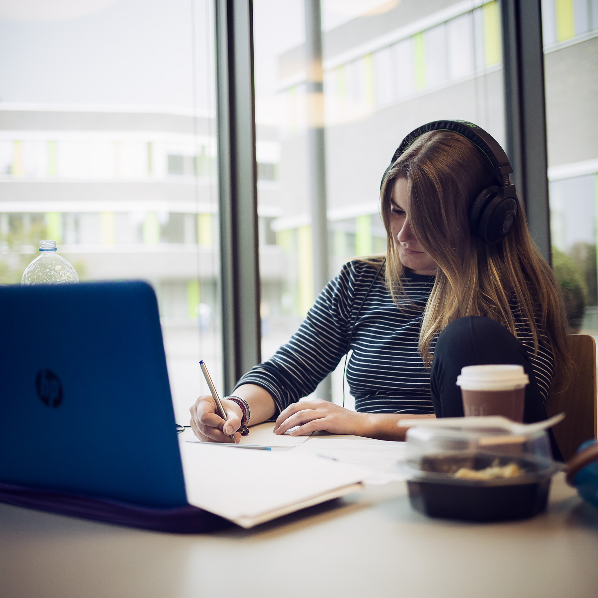 Studentin sitzt vor einem Laptop und schreibt etwas auf