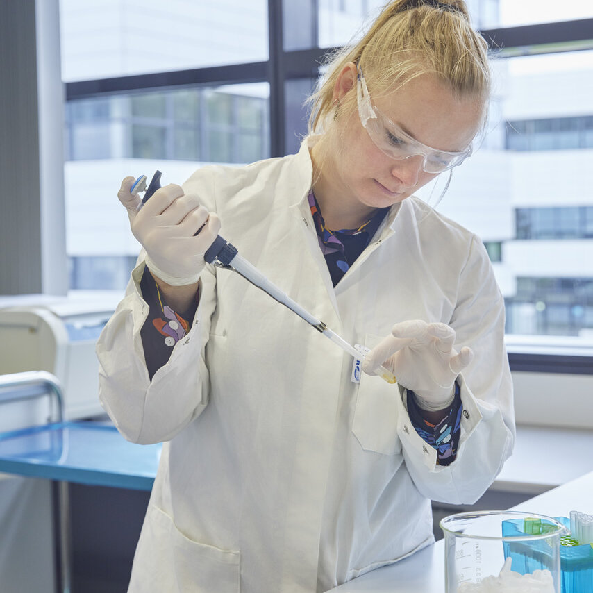 Die Professorin Prof. Dr. Natalie Laibach steht in einem Labor und trägt Kittel und Schutzbrille. Mit einer Pipette arbeitet sie an Proben.