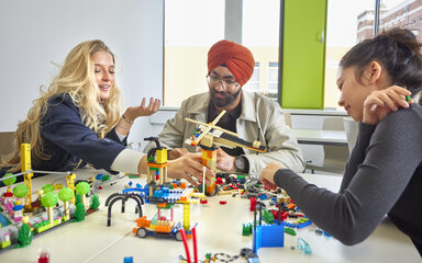 Drei Studierende sitzen gemeinsam an einem Tisch und arbeiten mit bunten Bausteinen.