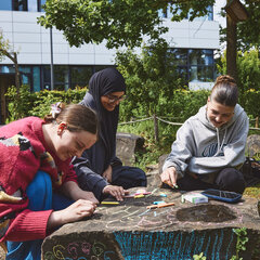 3 students are painting a boulder on the Kleve campus