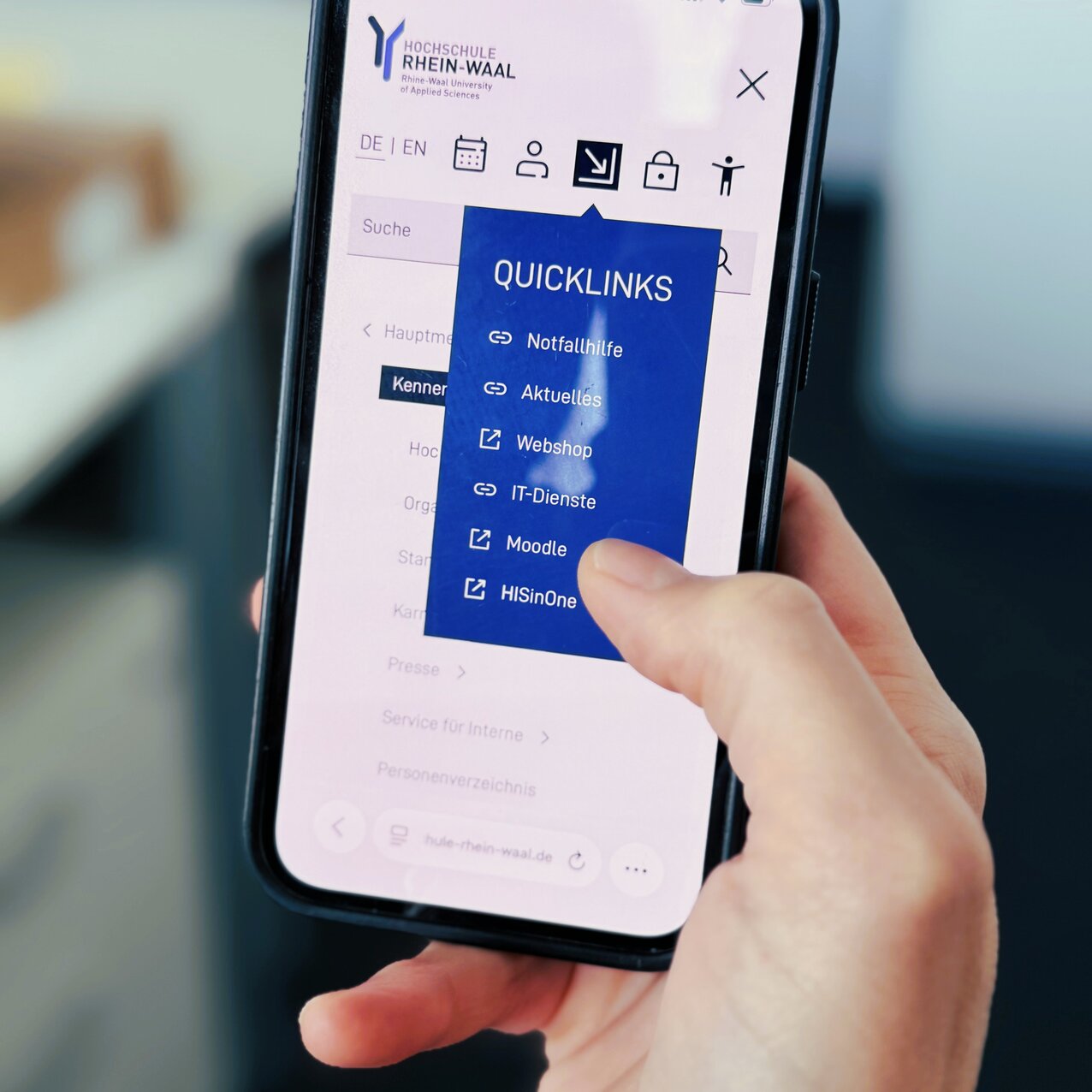 Someone is holding a mobile phone and selecting a Quicklink from the menu on the HSRW website.