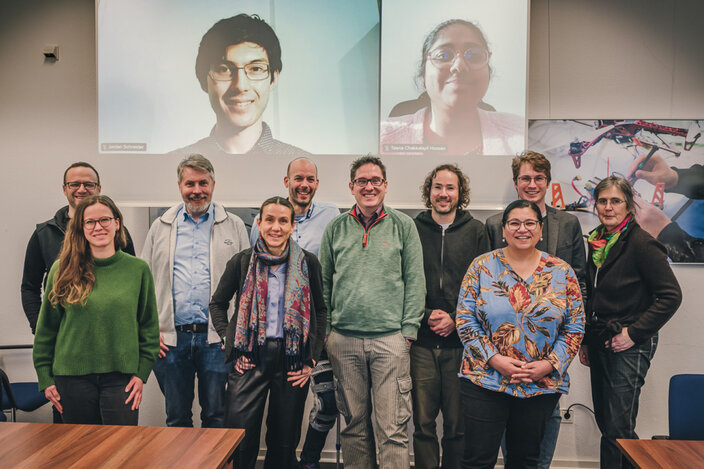 Online bzw. auf der Leinwand zu sehen (v.l.n.r.): Jordan Schneider (HBRS), Prof. Dr. Teena Hassan (HBRS)  Vor Ort (v.l.n.r.): Prof. Dr. Benedikt Janßen (HSNR), Anne Ferger (UDE), Prof. Dr. Thomas Nitsche (HSNR), Prof. Dr. Nele Wild-Wall (HSRW), Prof. Dr. Bernhard Breil (HSNR), Prof. Dr. Christian Ressel (HSRW), Dr. André Krause (HSRW), Iman Awaad (HBRS), Michael Stolarz (HBRS), Barbara Arntz (HSRW)