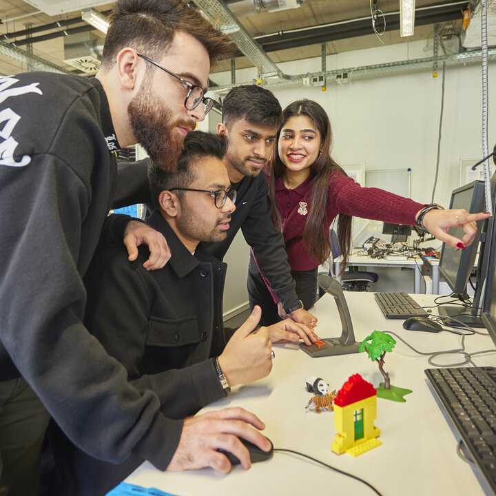 Four students are looking at a computer screen in the AIS Lab; one of them is pointing at it.