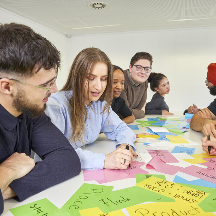 Students are sitting at a table covered in colourful sticky notes; some are writing on them.